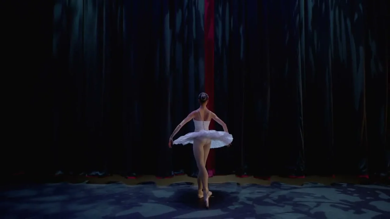 Ballerina en pointe alone on a dark stage before a red curtain