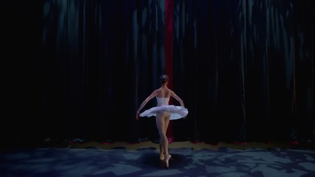 Ballerina en pointe alone on a dark stage before a red curtain